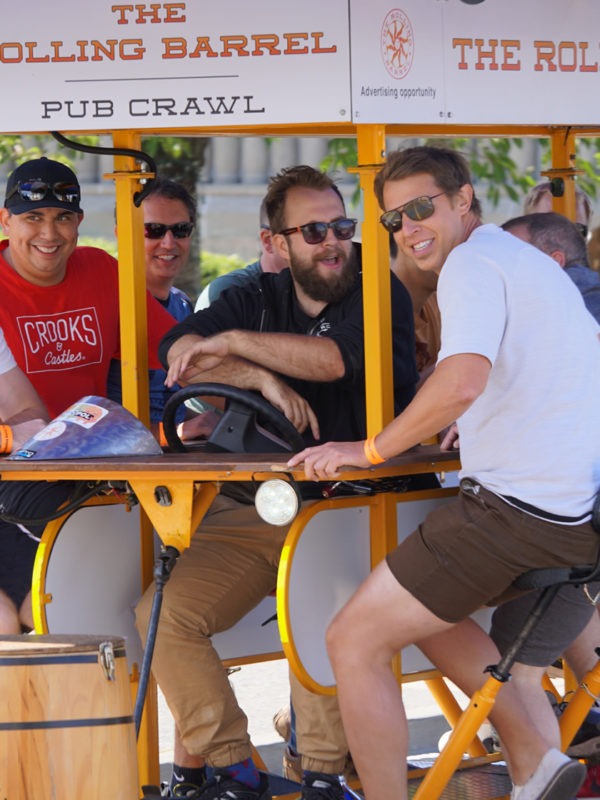 A group of happy men on tour and pedaling The Rolling Barrel vehicle with “Captain Mike” at the helm.