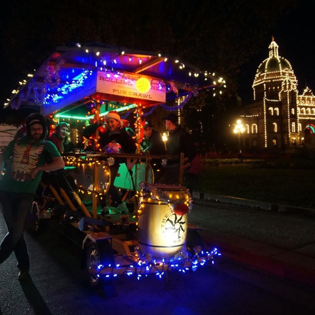 Night time front view of the Rolling Barrel vehicle decorated with Christmas lights and parked in front of the Victoria Parliament Building.
