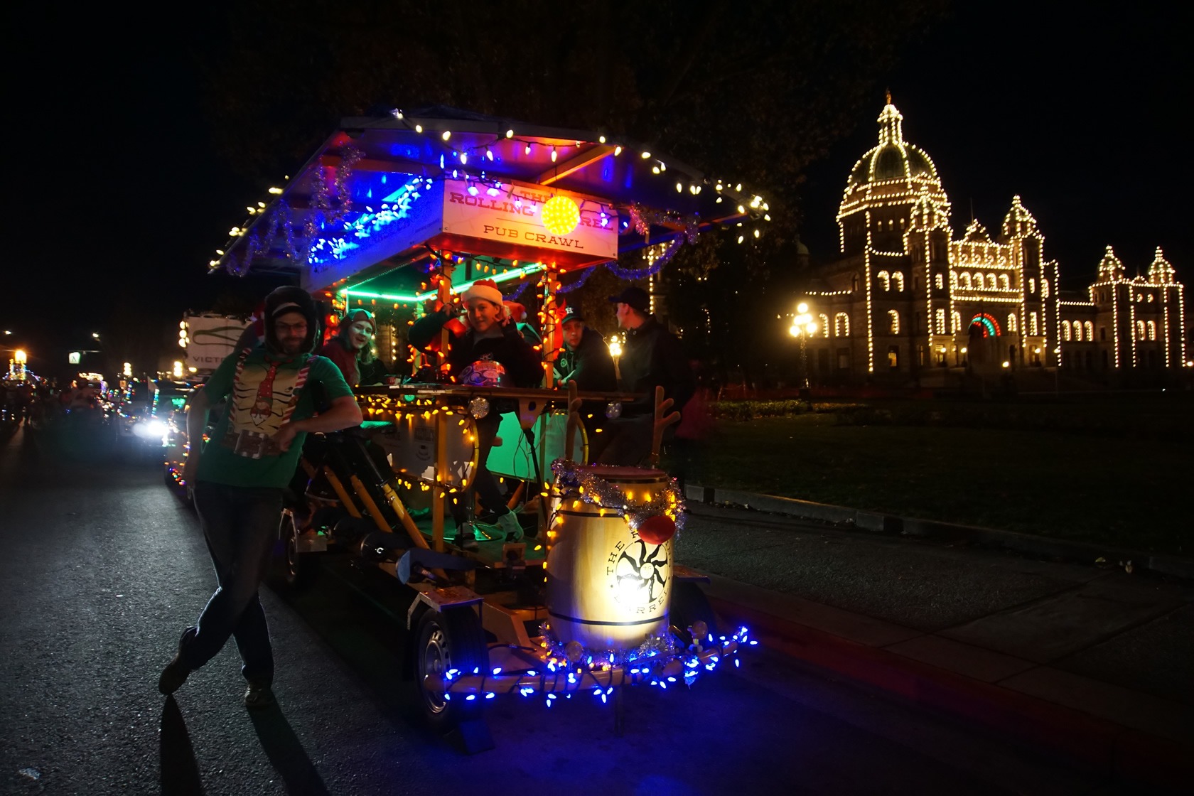 Night time front view of the Rolling Barrel vehicle decorated with Christmas lights and parked in front of the Victoria Parliament Building.
